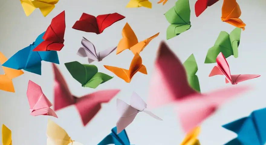 Papillons en origami multicolores flottant sur fond clair.