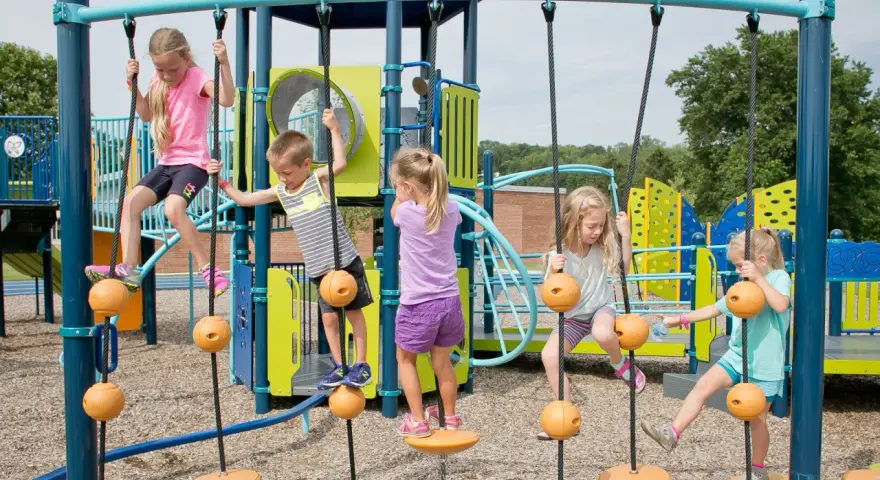 Enfants jouant sur une structure d'escalade avec des cordes et des balles oranges.