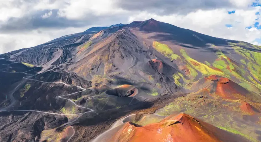 Vue aérienne de l'Etna, avec ses cratères rouges et ses pentes noires et vertes.