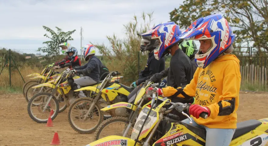 Jeunes pilotes prêts pour une course de moto cross. Casques colorés et motos jaunes alignées.