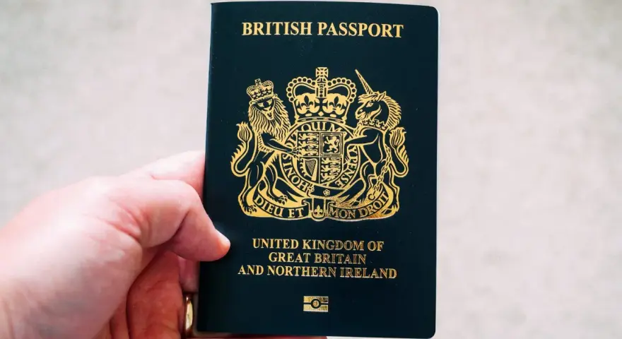 Main d'une personne tenant un passeport britannique bleu foncé avec le blason royal doré.