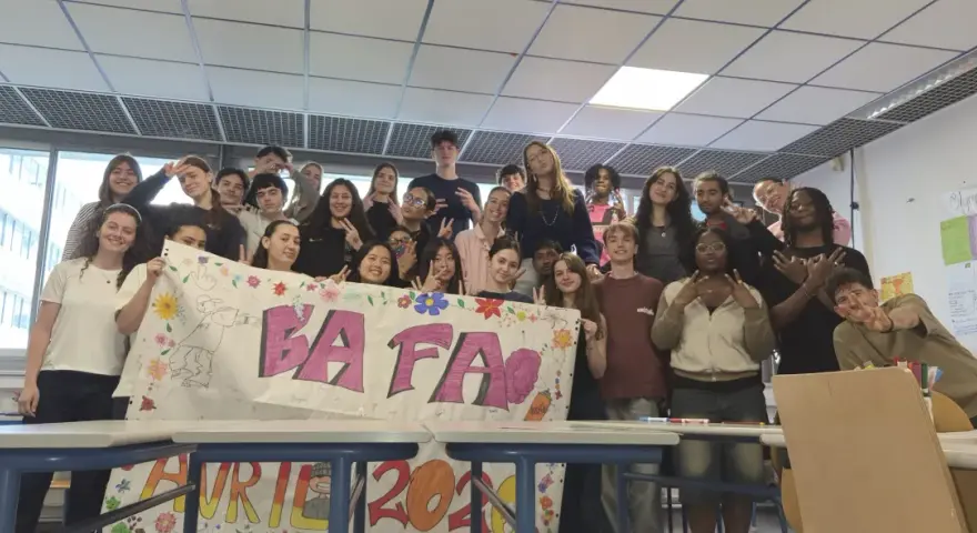 Un groupe d'étudiants pose derrière une banderole "BAFA" décorée de dessins et de fleurs.