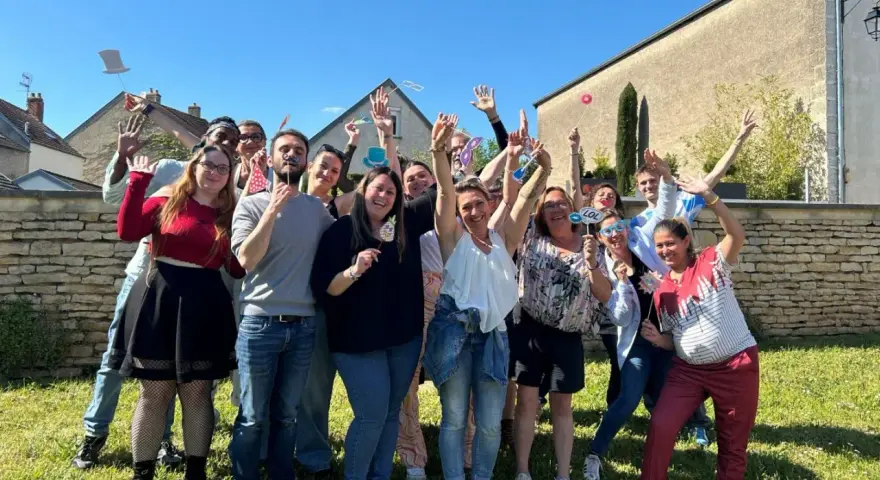 Groupe de personnes souriantes et joyeuses tenant des accessoires de photomaton, levant les mains en signe de salut.