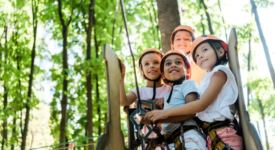 Quatre enfants souriants portant des casques de sécurité dans un parc d'aventure.