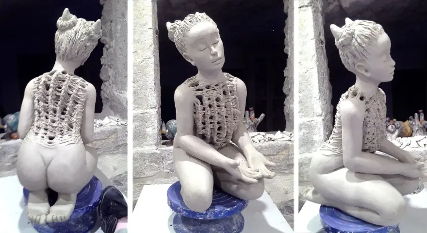 Sculpture en argile d'une jeune fille aux cornes, assise, vêtue d'une tunique ajourée.