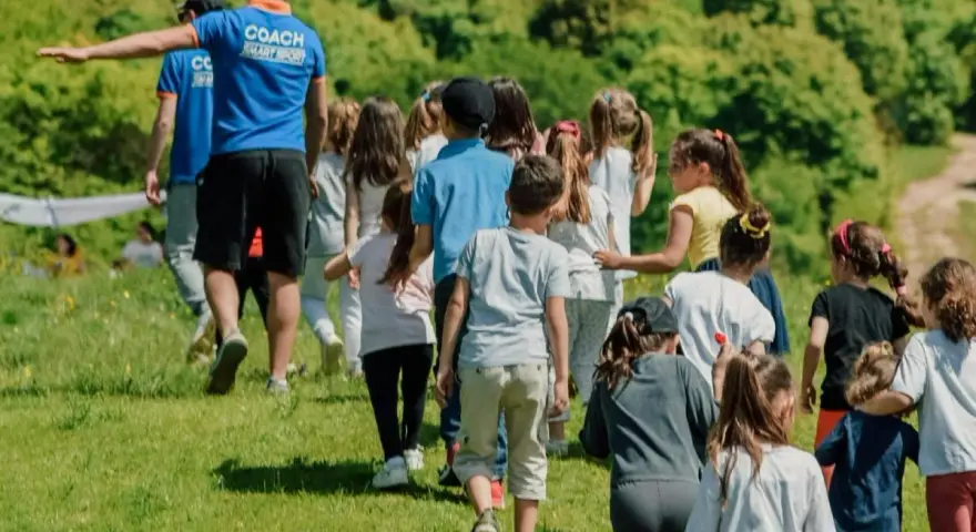 Un groupe d'enfants suit un coach sur une colline verdoyante. Ces actions pour financer un voyage scolaire sont pleines d'énergie et de joie.