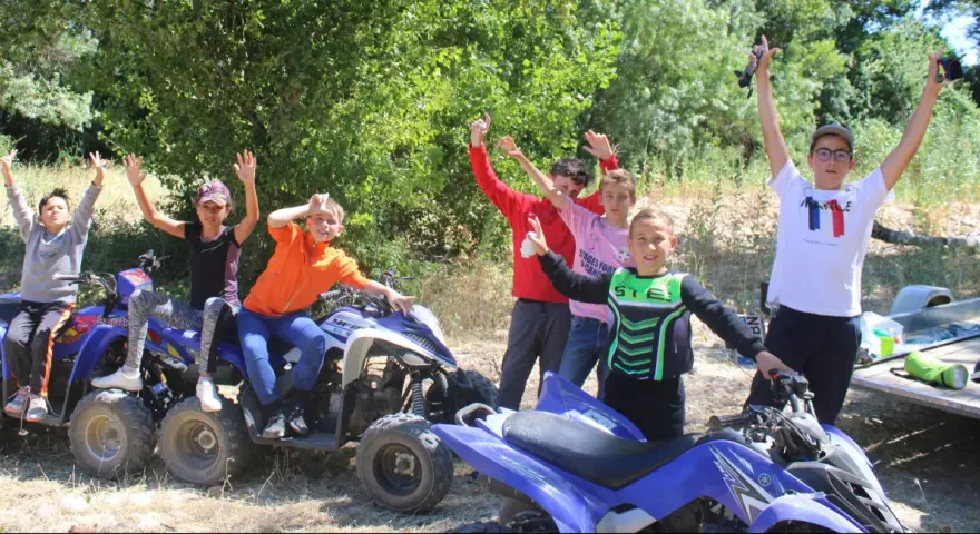 Des enfants joyeux sur des quads, bras levés, en extérieur.