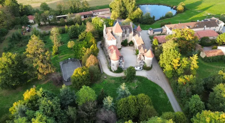 Vue aérienne d'un château entouré d'arbres, avec un étang et un terrain de sport.