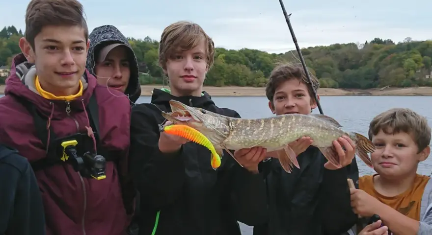 Des jeunes pêcheurs fiers de leur prise lors d'une colonie de vacances pêche. Un beau brochet exhibé devant un lac.