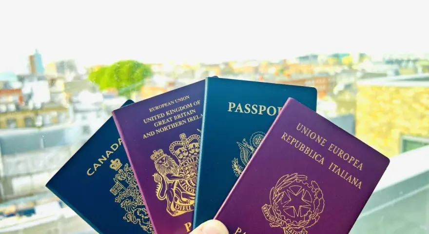 Plusieurs passeports (Canada, Royaume-Uni, UE, Italie) tenus devant un paysage urbain flou.