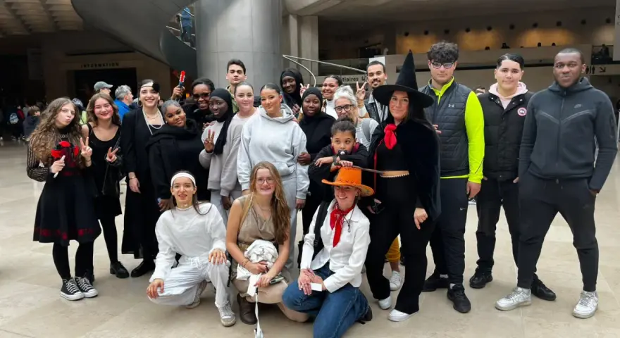 Un groupe de jeunes gens, certains déguisés, pose pour une photo dans un hall moderne.
