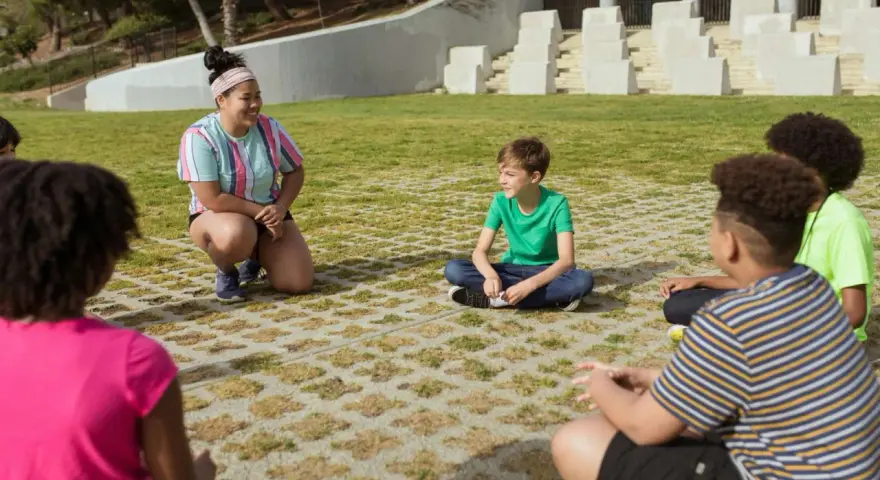 Une animatrice discute avec des enfants assis en cercle dans un parc.