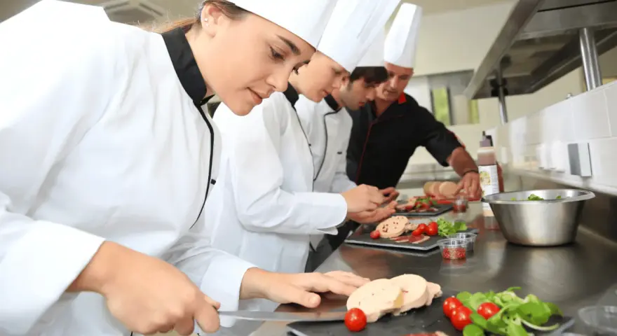 Des chefs apprennent la réglementation atelier cuisine en préparant des mets. Ils coupent du foie gras, des tomates cerises et de la salade.
