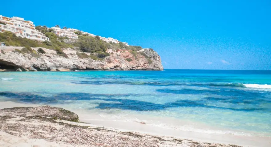Plage de Majorque avec eaux turquoises, falaises et bâtiments blancs à flanc de colline.