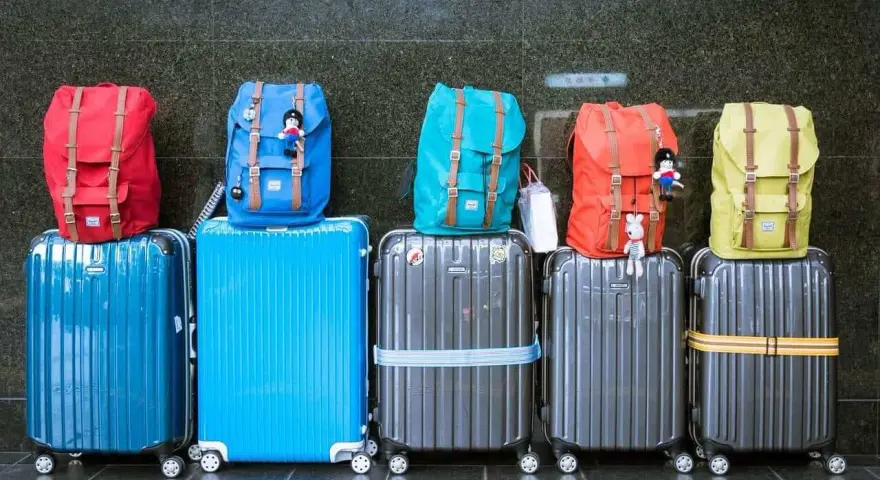 Six valises de différentes couleurs empilées, avec des sacs à dos colorés sur le dessus.
