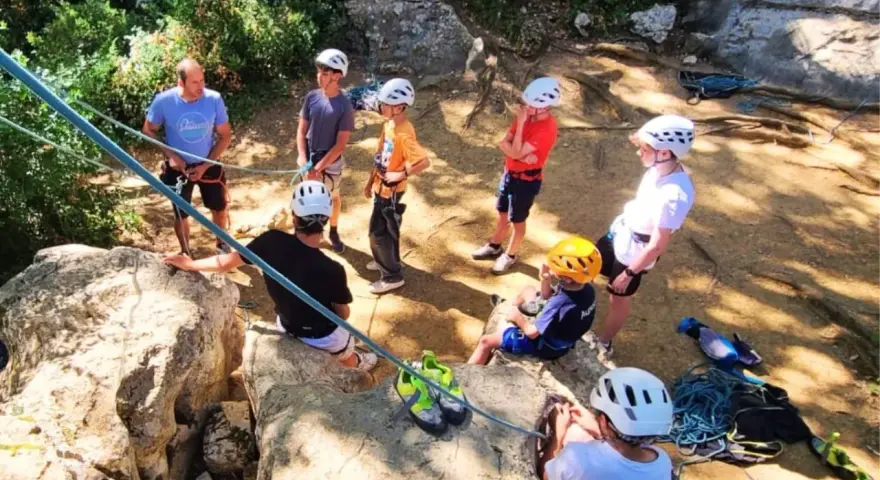 Des jeunes en pleine colonie de vacances escalade, casques blancs et jaunes, prêts pour l'aventure sur les rochers.
