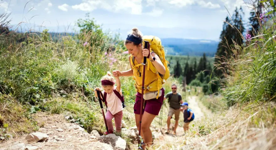 Famille faisant de la randonnée en montagne, une mère aide sa fille à monter un sentier.