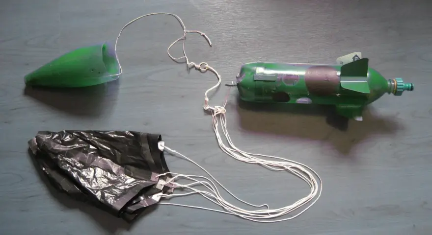 Fusée à eau verte avec cône, parachute noir et fils blancs sur fond gris.