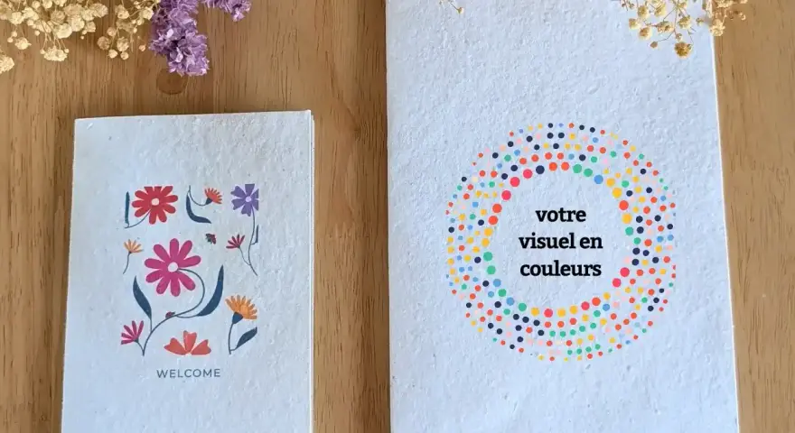 Deux carnets faits main sur fond de bois, décorés de fleurs et de points colorés.