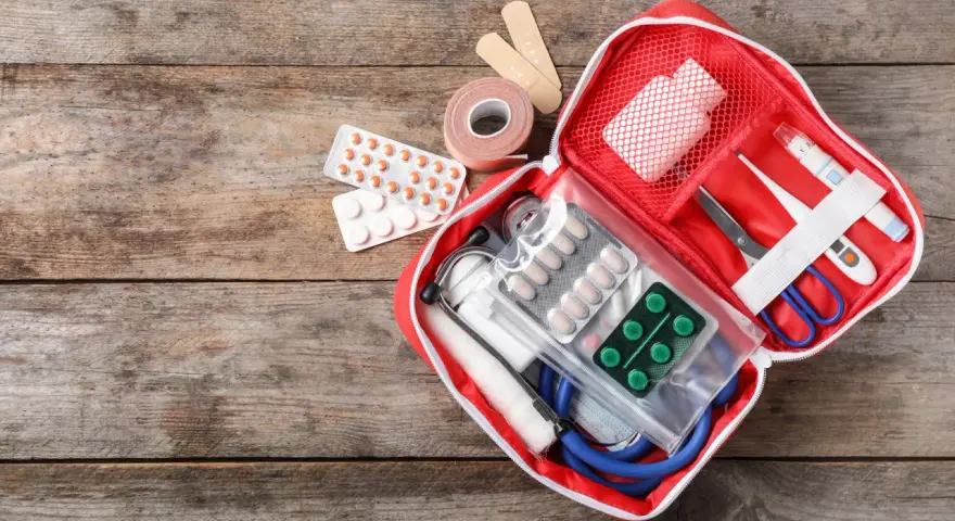 Trousse de secours pharmacie liste : pansements, rouleau de sparadrap, pilules, thermomètre, ciseaux, stéthoscope et masque.