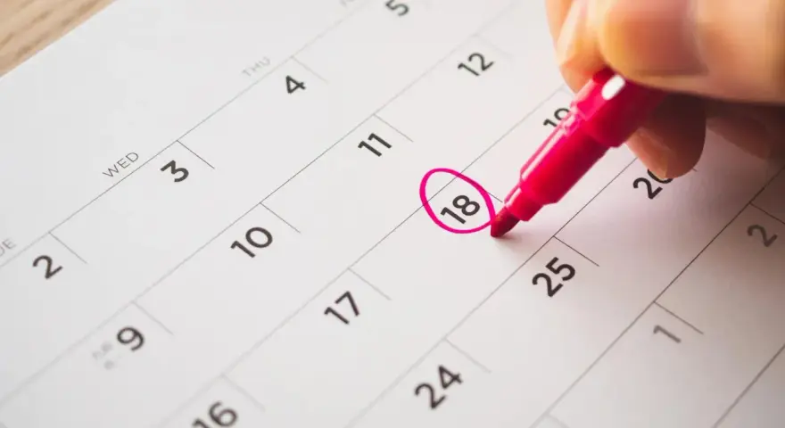 Une main entoure le 18 sur un calendrier, marquant le début des vacances scolaires à Fribourg.