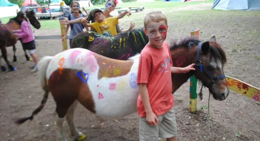 Enfants avec des poneys décorés de peinture, dans un campement avec des tentes.
