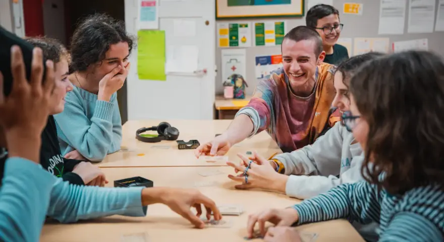 Des jeunes rient en jouant à un jeu de cartes autour d'une table.