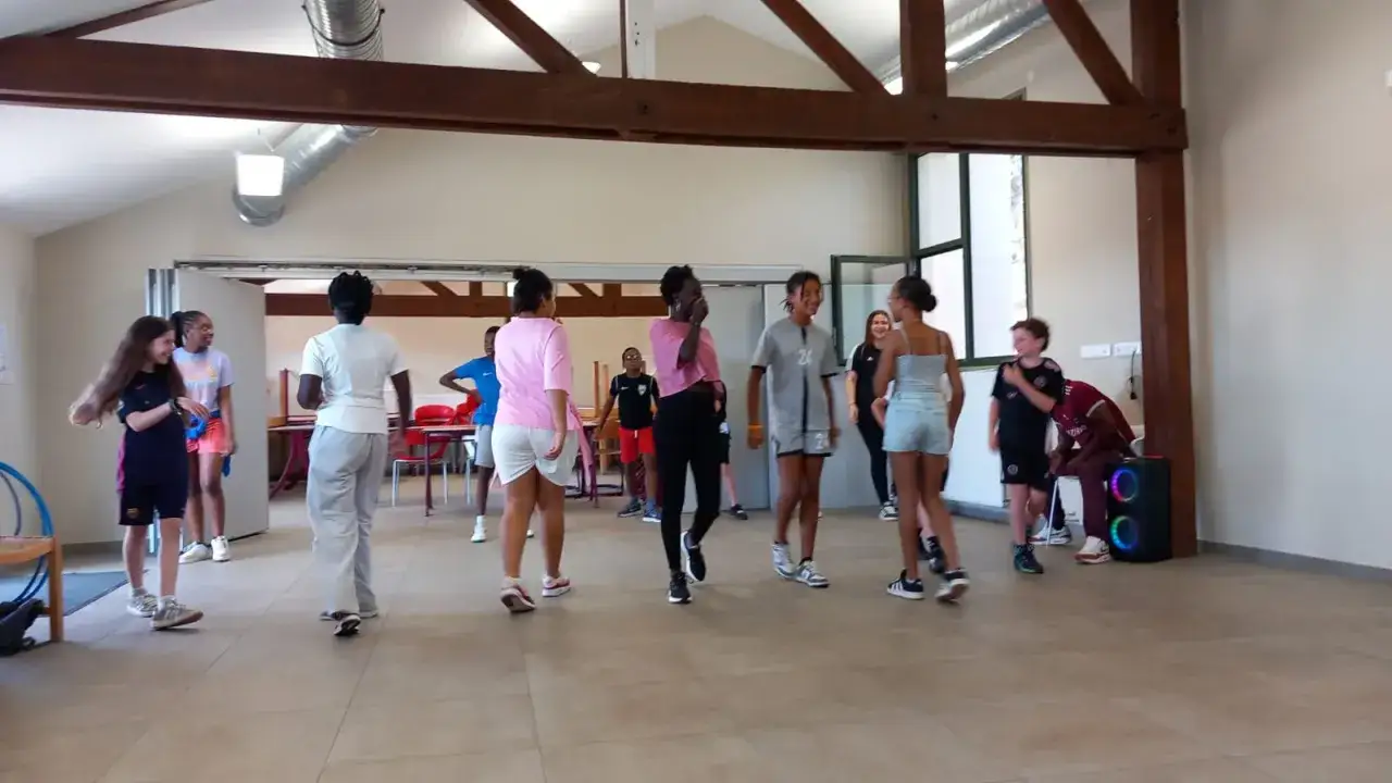 Des jeunes s'amusent lors d'une colonie de danse, certains dansent, d'autres observent, dans une grande pièce lumineuse.