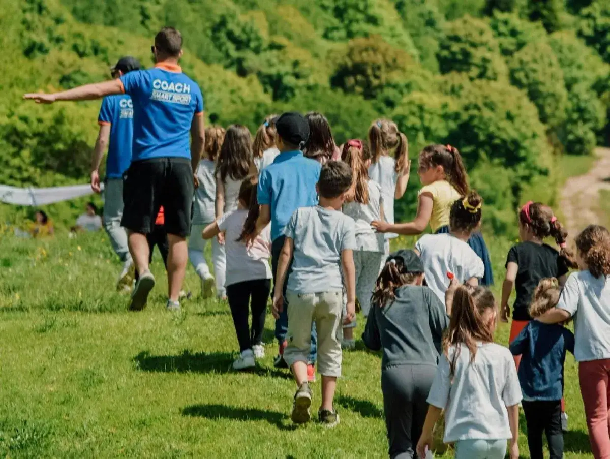 Un groupe d'enfants suit un animateur sur une colline verdoyante. Une belle journée pour apprendre comment financer un voyage scolaire.
