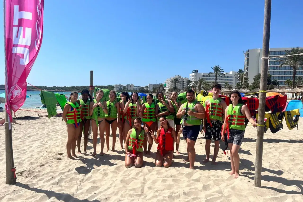 Groupe de jeunes souriants sur une plage, prêts pour une activité nautique lors de leur colonie de vacances à l'étranger.