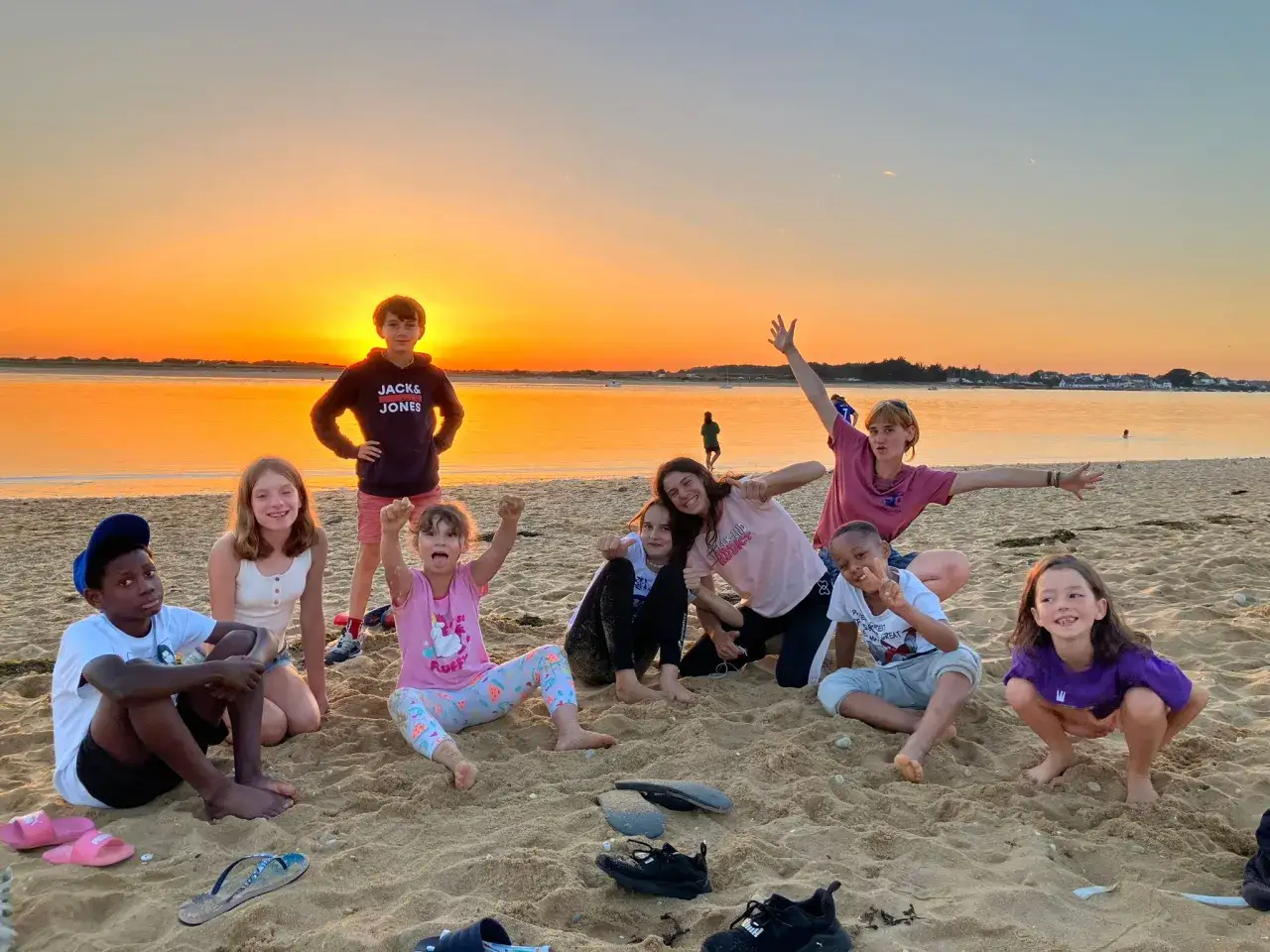 Des enfants joyeux profitent d'un coucher de soleil sur la plage, souvenirs d'une colonie de vacances camping inoubliable.