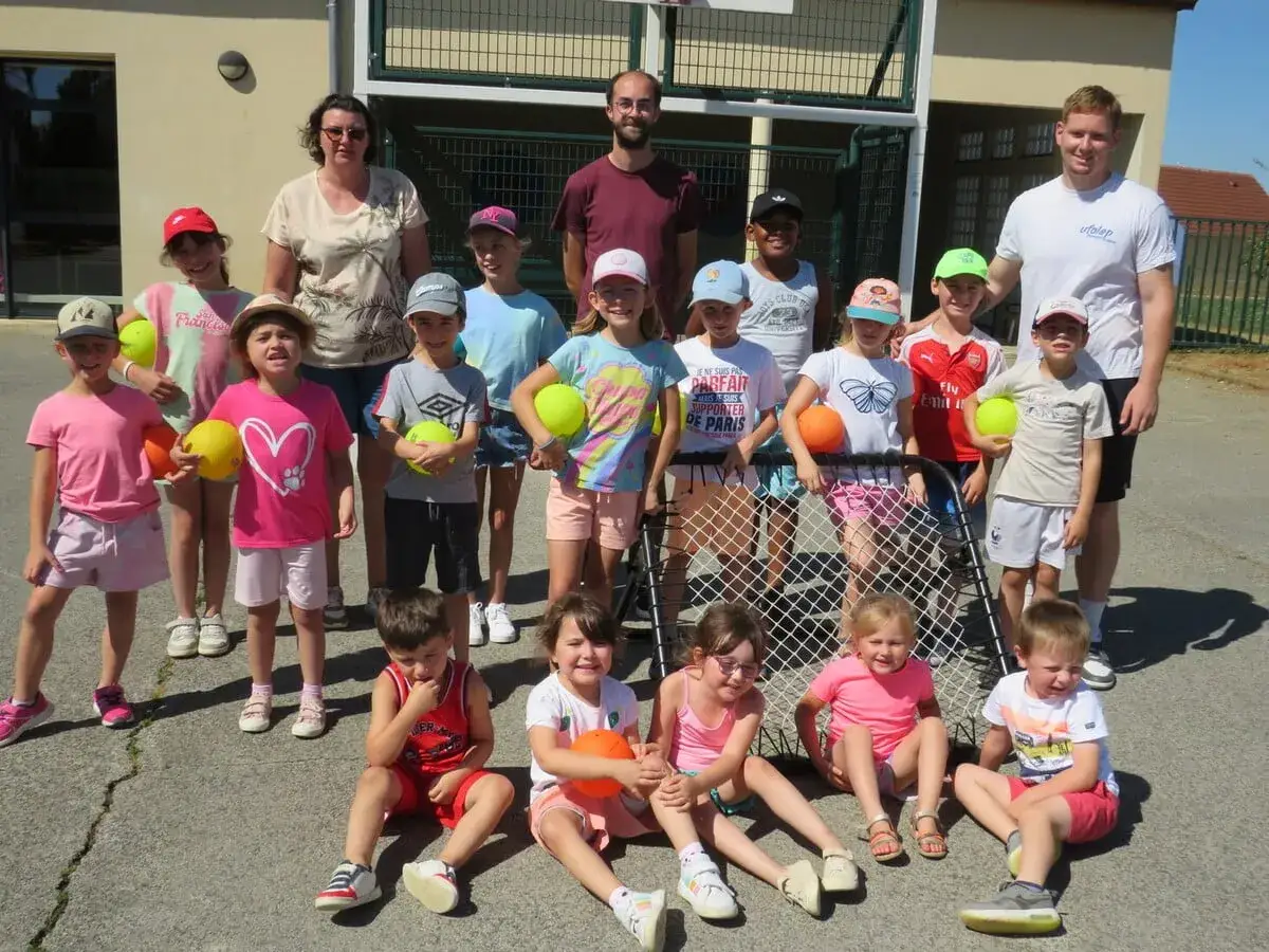 Le directeur du centre de loisirs pose avec des enfants joyeux, tous tenant des ballons colorés, prêts pour une journée d'activités sportives ensoleillée.