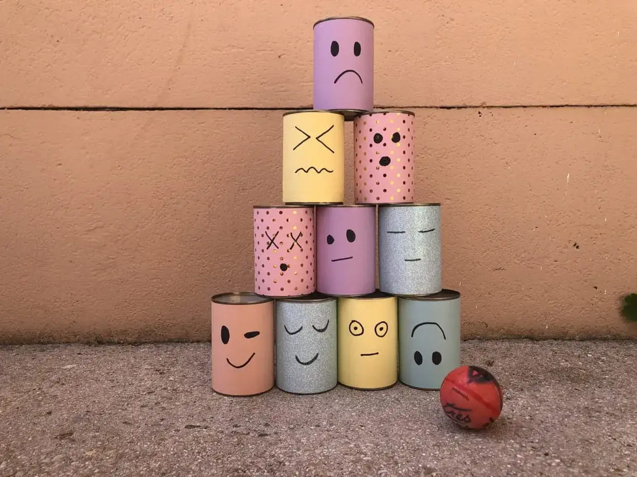 Pyramide de boîtes décorées de visages pour une kermesse chamboule tout. Un dessin amusant prêt à être renversé par une petite balle rouge.