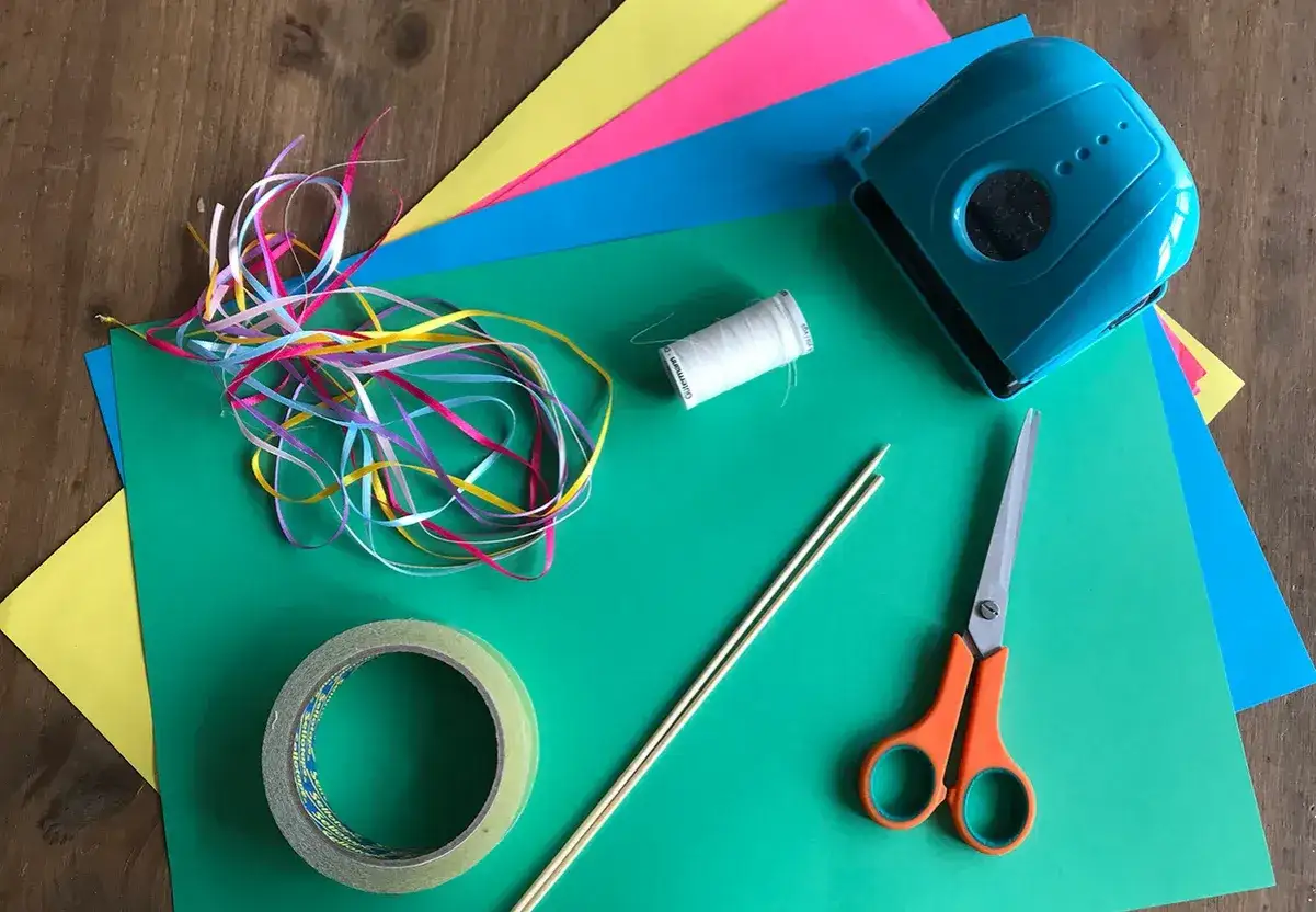 Matériel pour une activité manuelle : cerf volant en papier coloré, rubans, ciseaux, colle, fil et bâtons.