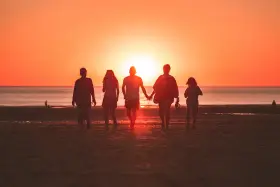 Une famille profite de ses vacances à l'étranger, marchant main dans la main sur une plage au coucher du soleil.