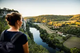 Une femme admire un paysage de carte postale lors de son voyage découverte en France. La rivière serpente à travers des collines verdoyantes et des villages pittoresques.