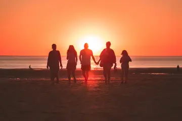 Une famille profite de ses vacances à l'étranger, marchant main dans la main sur une plage au coucher du soleil.