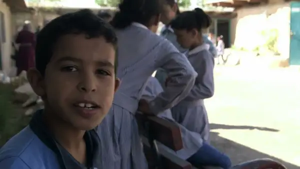 Un garçon souriant pose devant des filles en uniforme dans la même cour d'école.