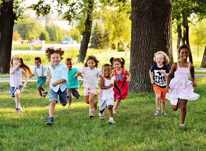 Des enfants joyeux courent dans l'herbe, profitant d'une journée ensoleillée dans une colonie de vacances 3-6 ans.