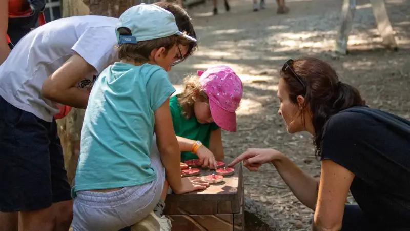 Une famille résout une énigme pour course d'orientation, manipulant des jetons sur un jeu en bois.