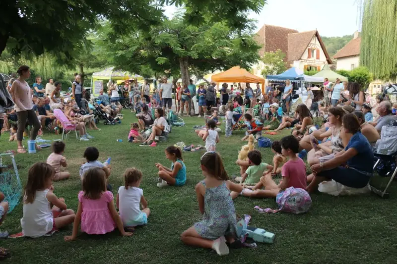 Une foule joyeuse, petits et grands, profite d'une fête de village. Une belle idée animation fête de village, avec des stands et des gens assis sur l'herbe.