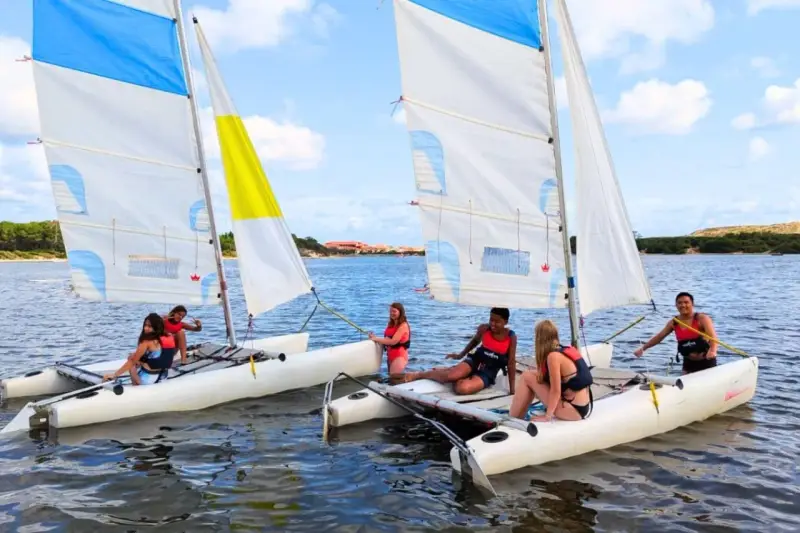 Des jeunes profitent d'une colonie de vacances voile, naviguant sur des catamarans par une journée ensoleillée.