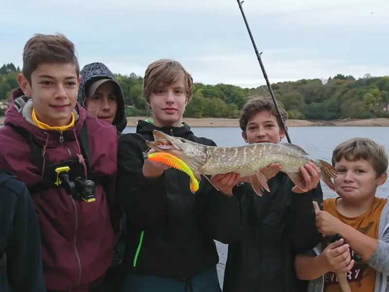 Des jeunes pêcheurs fiers de leur prise lors d'une colonie de vacances pêche. Un beau brochet exhibé devant un lac.